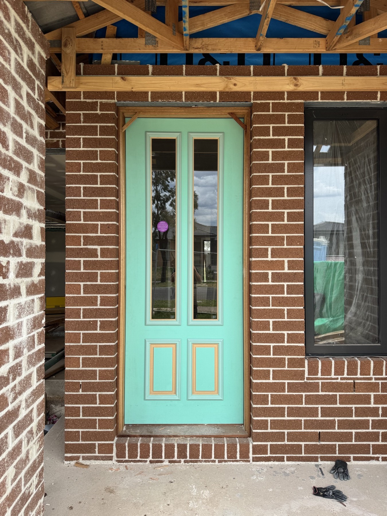 Mint green front door fitted in a brick entry with exposed timber framing above